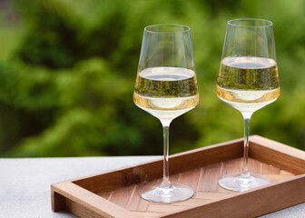 Two glasses of white wine presented on a wooden tray with garden background. Romantic celebration concept. Copy space.