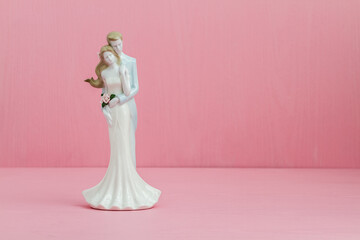 Porcelain wedding figurine of a couple embracing, set against a pink background, holding a bouquet of flowers, with copy space.