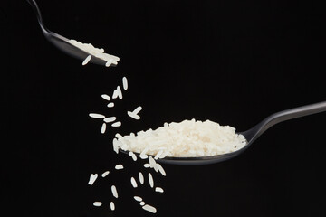 Falling rice grains from a  small spoon into a big spoon on a black background. Shallow depth of field