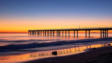 Fototapeta premium Tranquil sunset pier with city skyline silhouette reflected in waters, textured beach foreground