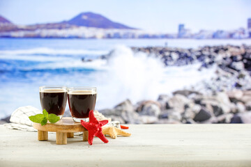 Glass cup of coffee on wooden stand on the beach with beautiful sea view in distance