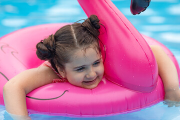Happy little child girl swimming with flamingo pink inflatable ring in clean pool water while having fun during vacation. Summer concept. Top view with copy space