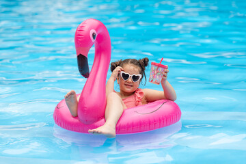 Cute child, little girl in sunglasses spend time in swimming pool on flamingo pink inflatable ring,...