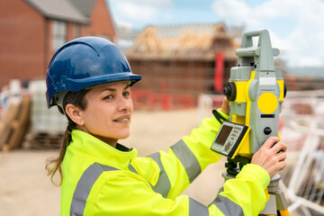 Happy smiling professional female site surveyor manager  works at building construction site with EDM total station instrument`