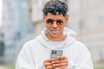 young man in sunglasses looking at mobile phone in the street