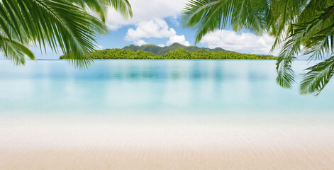 A Beautiful Tropical Beach with Clear Blue Waters, White Sands, Lush Green Mountains in the Background, and Palm Leaves in the Foreground, Suggesting a Serene and Peaceful Holiday Destination