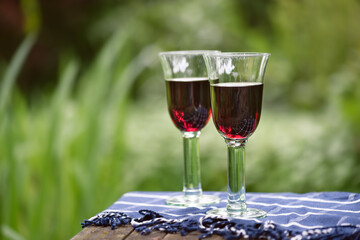 Two glasses of red wine on garden table garden background. Romantic celebration concept.  Alcoholic drinks. Camping. Picnic. Cold white wine. Rest for two. Warm evenings. Copy space.