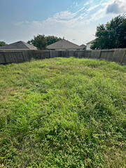 Abandoned looking house backyard with very overgrown grass surrounded by a old wood fence under a blue sky.