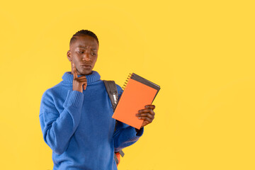 Young Woman in Sweater Holding Textbook and Thinking Against Yellow Background with Copy Space