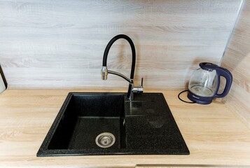 An elegant black kitchen sink with a sleek faucet sits next to a transparent glass kettle on a...