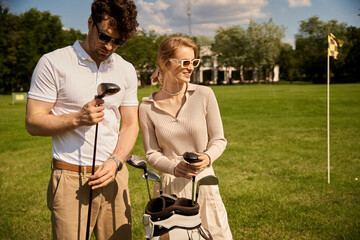 A young couple, elegantly dressed, stands together on a picturesque golf course, embodying a classic, upper-class lifestyle. © LIGHTFIELD STUDIOS