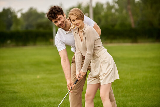 A young man and woman in elegant attire playing golf on a lush green field at an upscale club, embodying a high-class lifestyle.