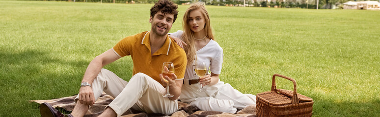 Elegant couple in stylish attire enjoying a leisurely moment on a picnic blanket amidst a lush park...