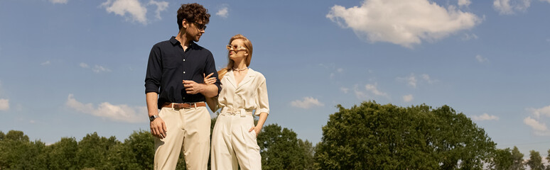 A beautiful young couple in elegant attire standing gracefully in a lush green field, embodying a...