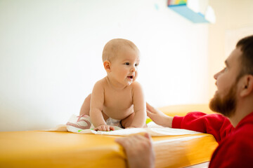 A baby is sitting in a diaper  on a couch in a hospital with dad. Father and baby in hospital. 