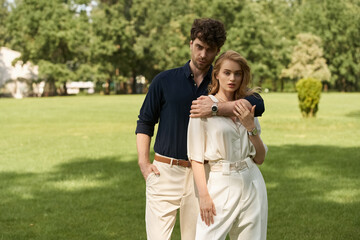 Elegant couple in fashionable attire enjoying a day at the park surrounded by lush greenery.