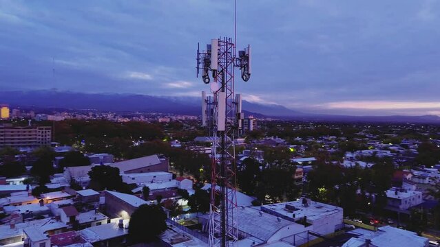 Cellphone communications tower in the city at dawn. Aerial view, orbit motion.