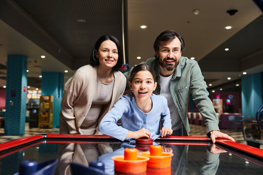 A happy family competes in a game of air hockey at an arcade, laughing and enjoying a fun weekend together.