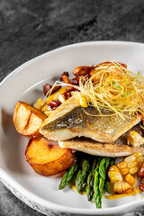 Seared fish atop roasted potatoes, garnished with herbs, served in a white bowl on a textured grey surface