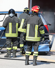 Three firefighters in uniform with helmets extinguish the fire of car after the car accident with the hose on the road