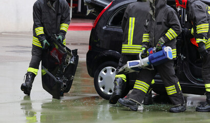firefighter using powerful pneumatic shears to pry open the jammed door of a wrecked car after a...