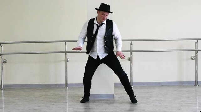 Rhythmic dance cha cha or bachata. Handsome young dancer in creative jazz clothes. Modern Dancer in a hat with a tie and a black vest, against the background of a wall