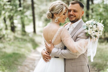 Wedding couple bride and groom hugging in pine forest, sunlight filtering through the trees,...