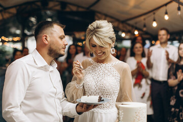 The wedding cake. The bride and groom cut off a piece of cake with a knife. The hands of the newlyweds cut the first piece of the wedding cake.