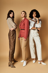 Three young, beautiful women in stylish clothes stand side by side against beige background, showcasing diversity in cultures.