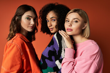 Three young, multicultural women stand stylishly before a vibrant red backdrop, showcasing diversity in fashion and culture.