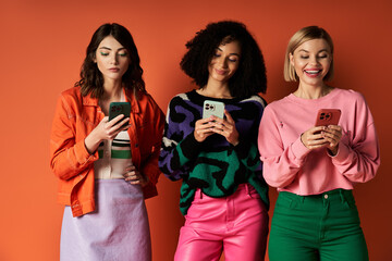 Three young, beautiful women in stylish clothes, displaying diversity in culture, pose together against an orange background.