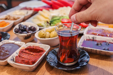 A close-up shot of traditional Turkish tea being stirred, surrounded by an array of breakfast items including olives and spreads.
