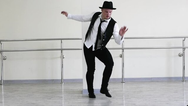 Rhythmic dance cha cha or bachata. Handsome young dancer in creative jazz clothes. Modern Dancer in a hat with a tie and a black vest, against the background of a wall
