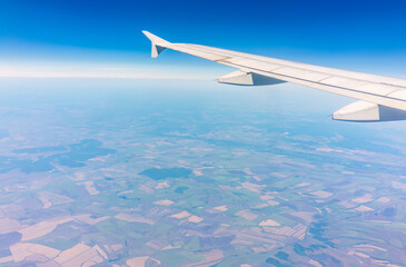 Obraz premium Aerial view from airplane window above green ground. View from the airplane window with beautiful clouds at sunrise