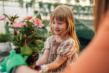 Naklejka premium Portrait of cute little florist planting flowers at hothouse with mom.