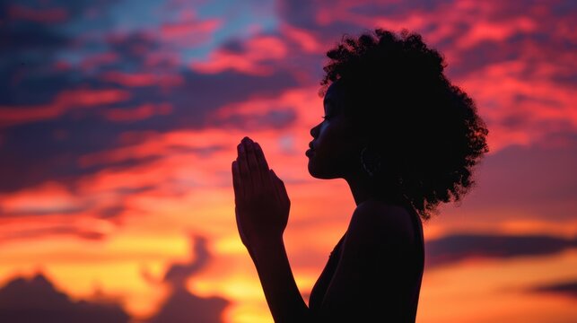A silhouette of a woman in prayer position against the backdrop of a beautiful sunset, ideal for use in devotionals or inspirational quotes