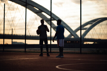Two men talking on basketball court at dusk