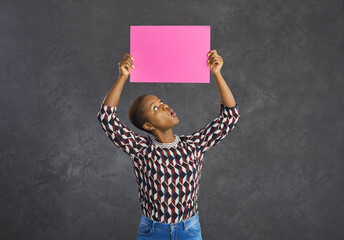 Funny dark skinned woman looking at a pink blank sheet of paper that she is holding over her head....