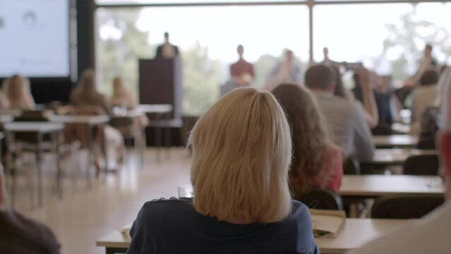 People sitting indoors, back view. Conference participants are seated indoors, viewed from the back, attentively listening to a speaker.