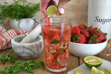 Squeezing lime juice into Strawberry mojito cocktail drink with lime, white rum, moscato,...