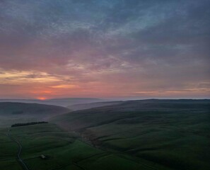 The vibrant colors of the sunset sky paint a dramatic backdrop over the Arncliffe countryside landscape