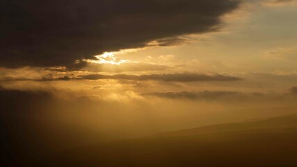 Sun rays break through the cloud cover, casting a soft, golden light over the landscape near Arncliffe