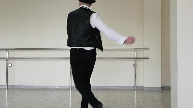 Rhythmic dance cha cha or bachata. Handsome young dancer in creative jazz clothes. Street Dancer in a hat with a tie and a black vest and jazz shoes, against the background of a wall.