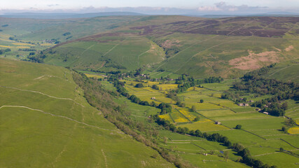 Aerial view of a quaint Yorkshire Dales village nestled among vibrant buttercup meadows, showcasing the scenic beauty and tranquility of the Dales