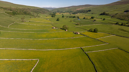 A breathtaking aerial panorama of the Yorkshire Dales, featuring meadows of buttercups, stone structures, and winding walls
