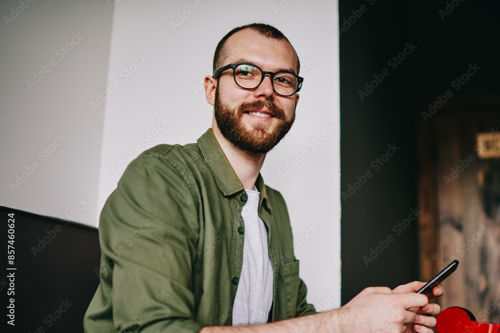 Poster portrait of handsome hipster man distracted from work on laptop, freelancer holding mobile phone for