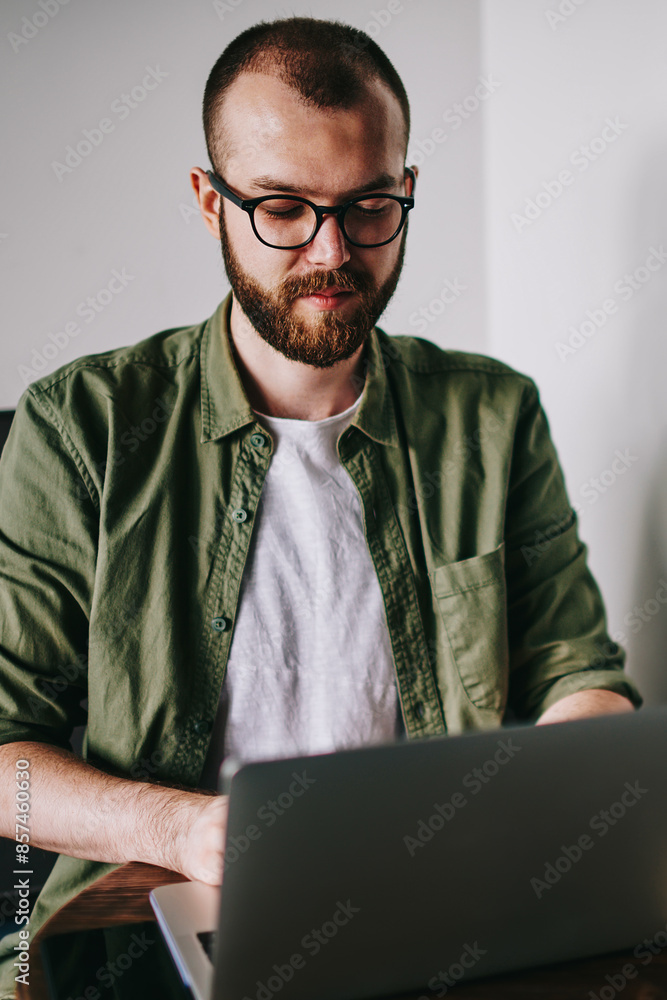 Poster handsome it developer in casual wear and eyeglasses using laptop at cafe professional typing some se