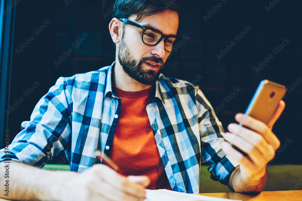 Aufkleber pensive bearded student rewriting text information from smartphone device in notepad.hipster guy in 