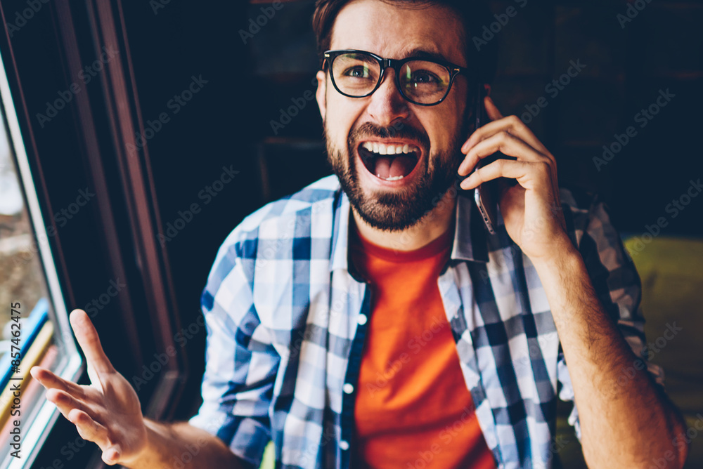 Poster top view of angry bearded hipster guy dressed in casual outfit shouting during phone call on digital