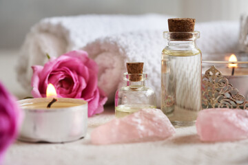 Two bottles of aromatherapy essential oil with rose de Mai flowers, rose quartz stones and spa towels